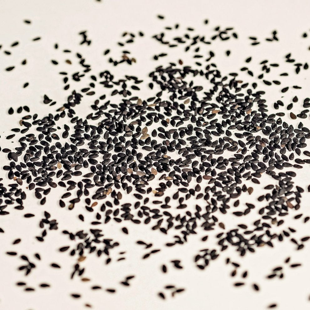 Schwarzer Sesam, ungeschält, lose verstreut auf einer weißen Oberfläche. Nährstoffreiche Zutat für die asiatische & gesunde Küche.