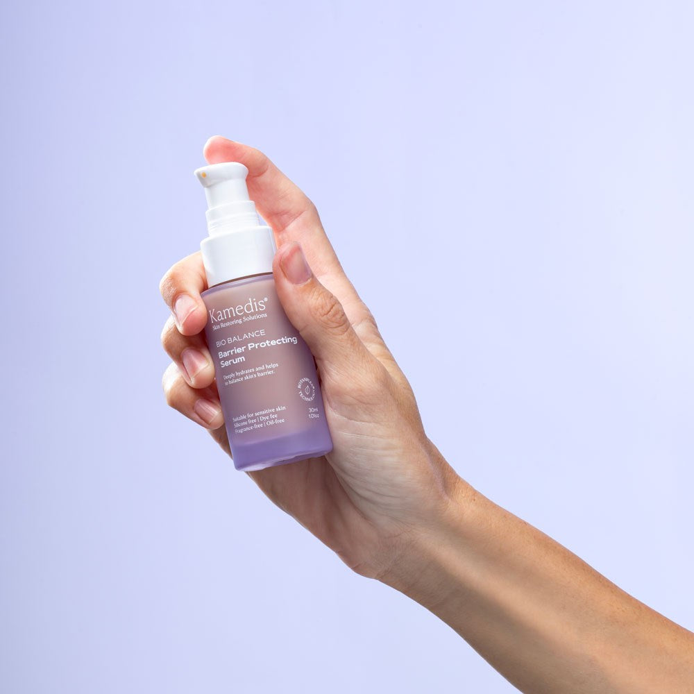 Hand hält eine violette Airless-Pumpflasche Kamedis Bio Balance Barrier Protecting Serum, geeignet für empfindliche Haut.