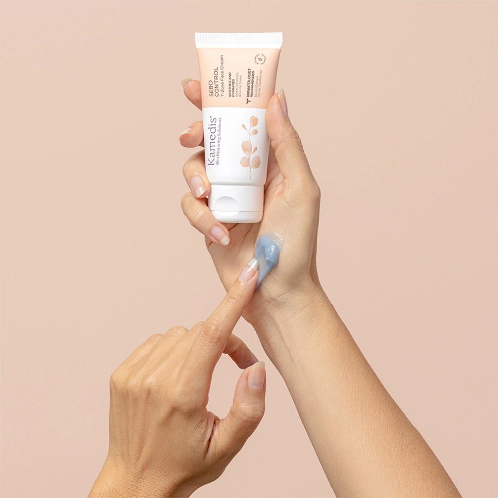 Hand hält eine Tube der Kamedis Sebo Control Cream, während eine blaue Gel-Textur auf den Handrücken aufgetragen wird. Hautpflege für fettige, unreine Haut.
