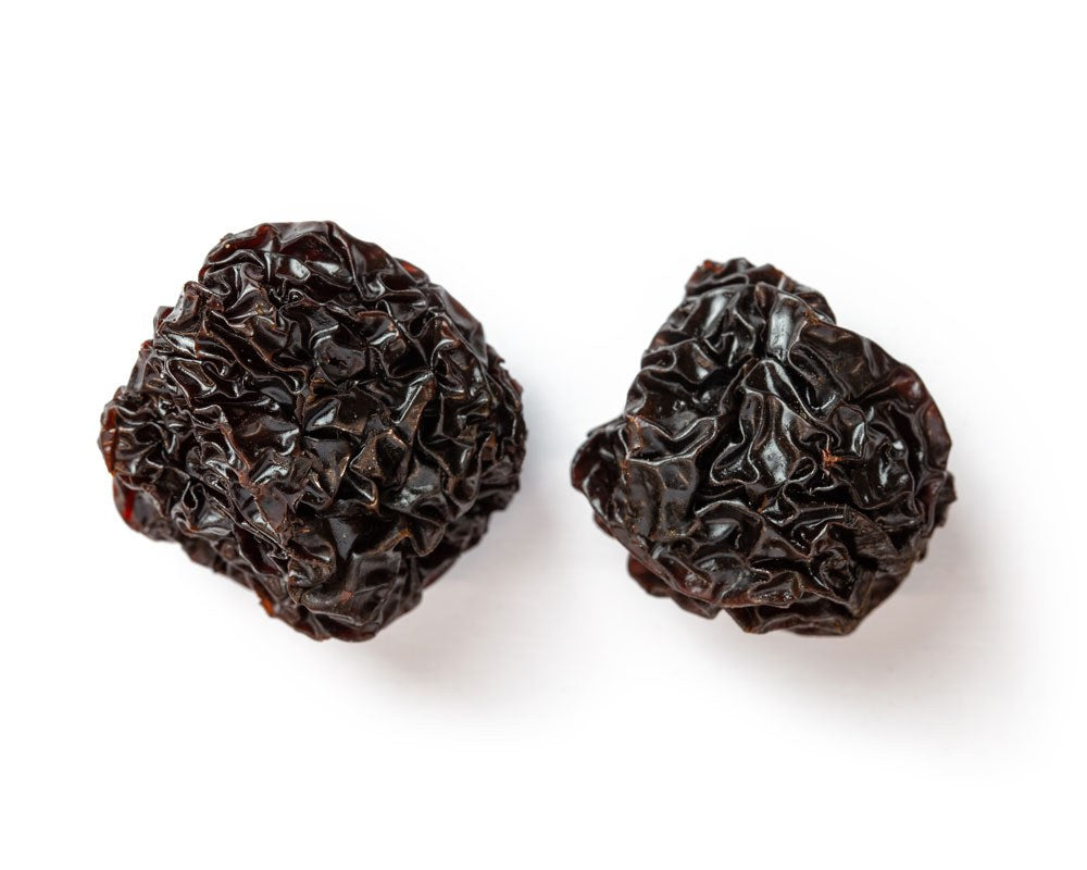 Zwei schwarze chinesische Datteln, die ihre natürliche Struktur und dunkle Farbe zeigen, auf weißem Hintergrund.