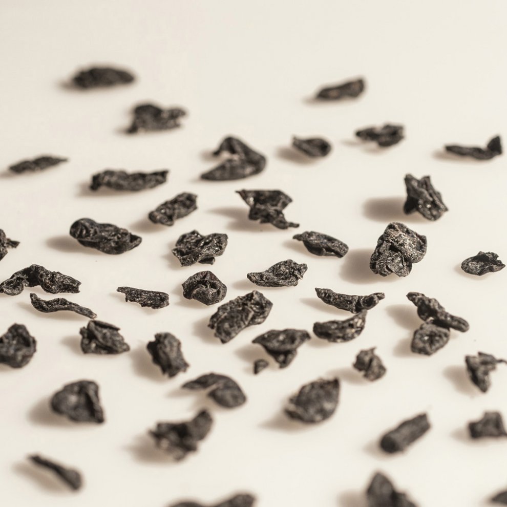 Getrocknete Stücke der Chinesischen Kornelkirsche (Shan Zhu Yu) auf einer weißen Oberfläche. Dunkle, leicht schrumpelige Textur.